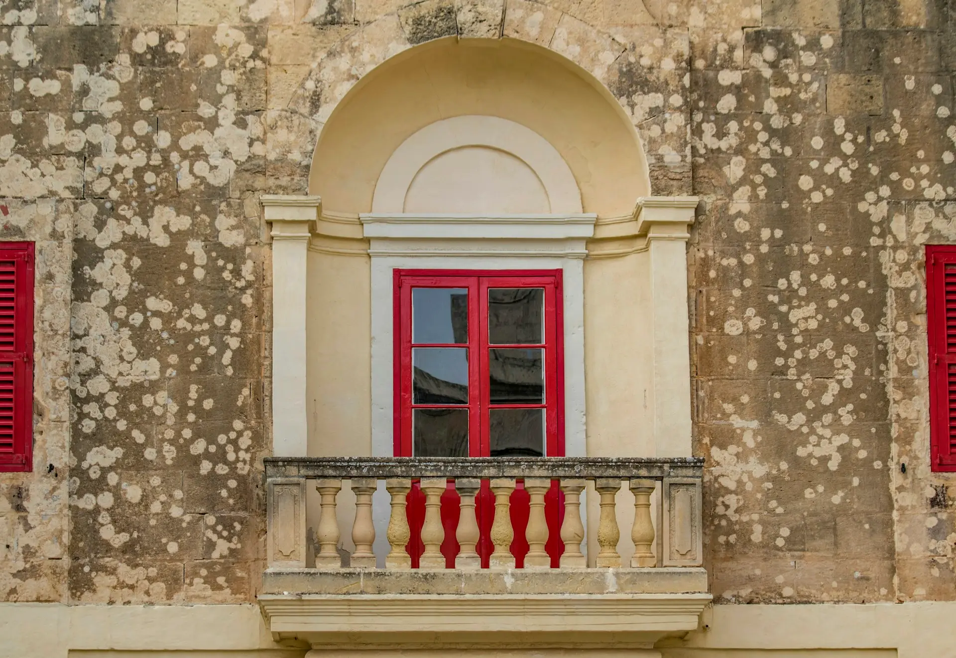 Rotes Fenster mit Steinbalkon in einer verwitterten Kalksteinfassade