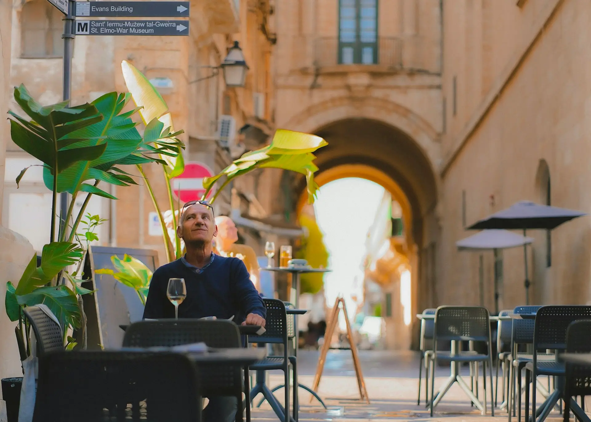 Mann an einem Cafétisch in einer Gasse in Valletta unter einem Torbogen