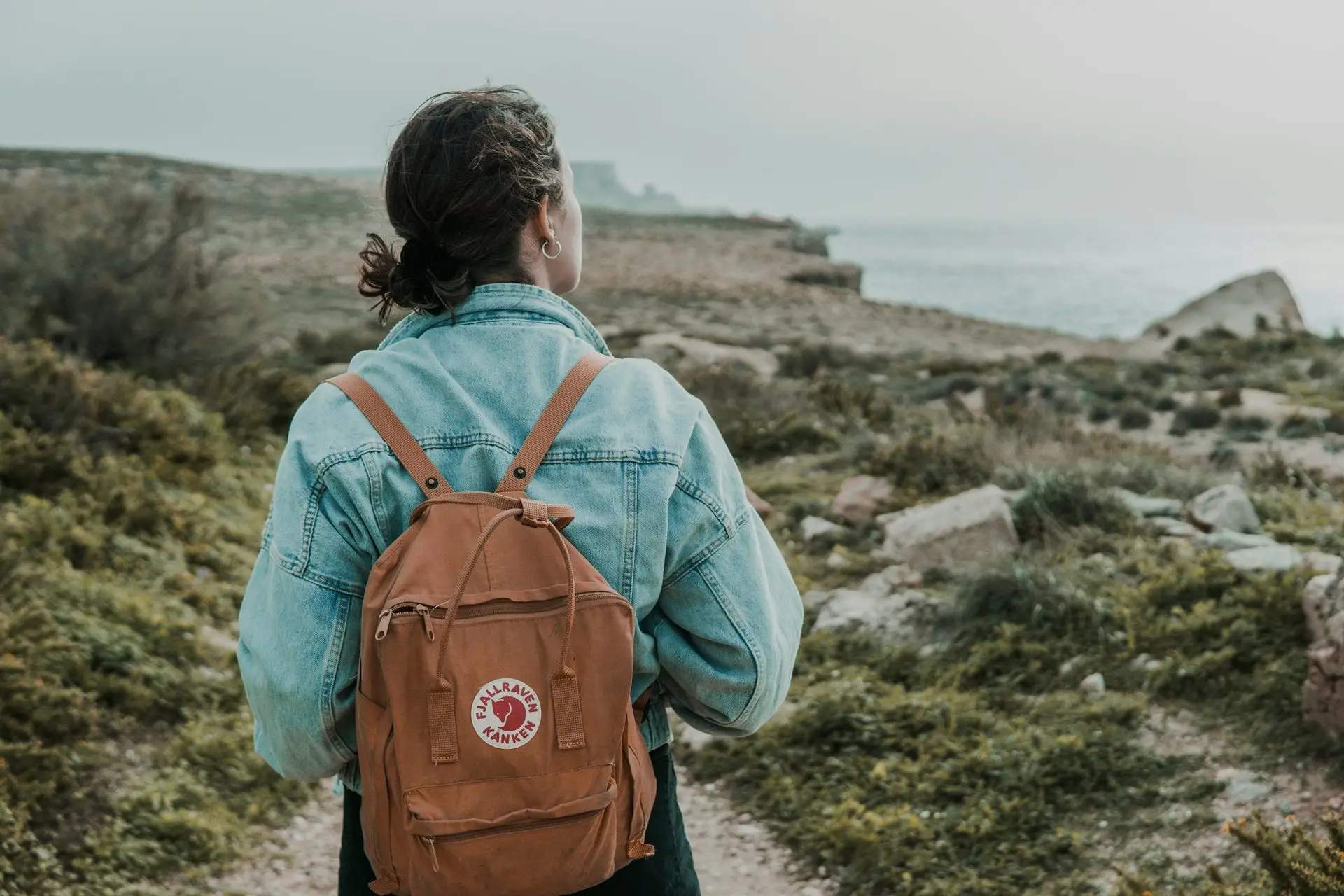 Wanderin mit Rucksack von hinten auf einem Küstenpfad