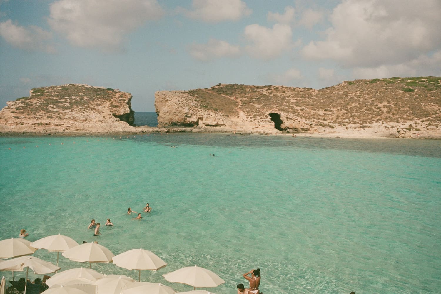 Badegäste im türkisfarbenen Wasser der Blue Lagoon auf Comino, am Ufer Sonnenschirme